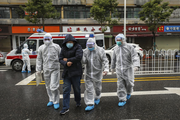 In Wuhan, on January 26, medical workers in protective gear help a patient from an ambulance. 