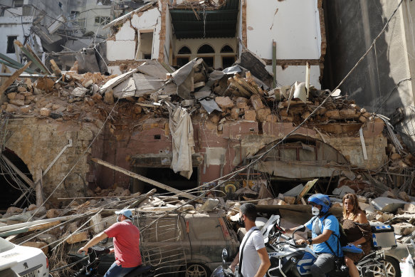 Citizens ride their scooters and motorcycles pass in front of a house that was destroyed .