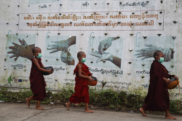 Buddhist novice monks wearing face masks walk past a COVID-19 awareness sign as they collect morning alms in Yangon on Thursday.
