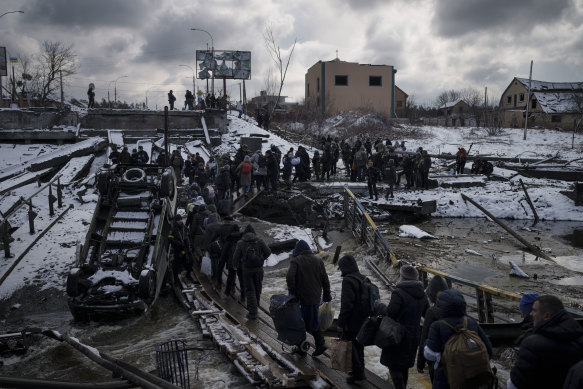 Ukrainians cross an improvised path under a destroyed bridge while fleeing Irpin.