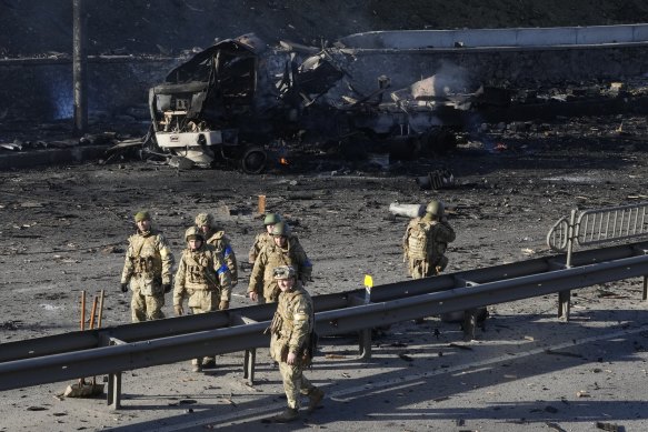 Ukrainian soldiers walk past the debris of a burning military truck on a street in Kyiv, Ukraine on Saturday.
