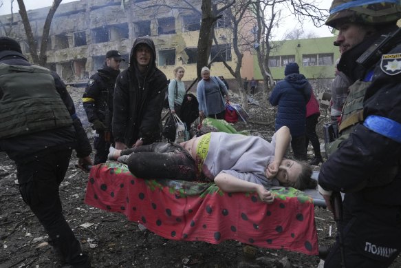 An injured pregnant woman is carried away from the maternity hospital, which was damaged by Russian forces on Thursday (AEDT).
