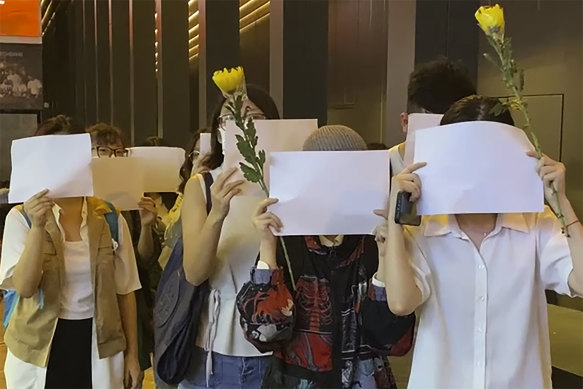 Students in Hong Kong chant “oppose dictatorship” while others hold up blank paper during a vigil for the Urumqi fire victims on Monday. 
