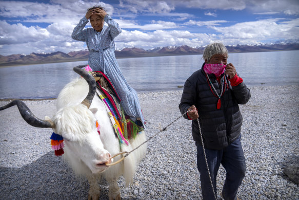 A Chinese tourist prepares to pose for a photo atop a white yak being led by a Tibetan man in Namtso.