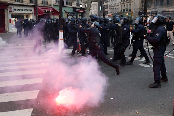 Protesters and riot police stand amidst tear gas.