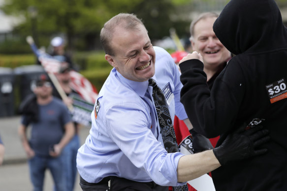Initiative promoter and gubernatorial candidate Tim Eyman disregards social distancing guidelines as he leans in to place a sticker on a child's back at a protest opposing Washington state's stay-home order on Sunday.