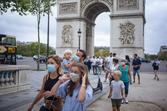 A family walks along on the Champs-Elysees avenue, with the Arc de Triomphe in the background.
