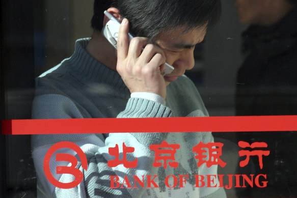 A man uses his mobile phone near the logo for the Bank of Beijing. The state-owned bank’s former chairman is under investigation for corruption.