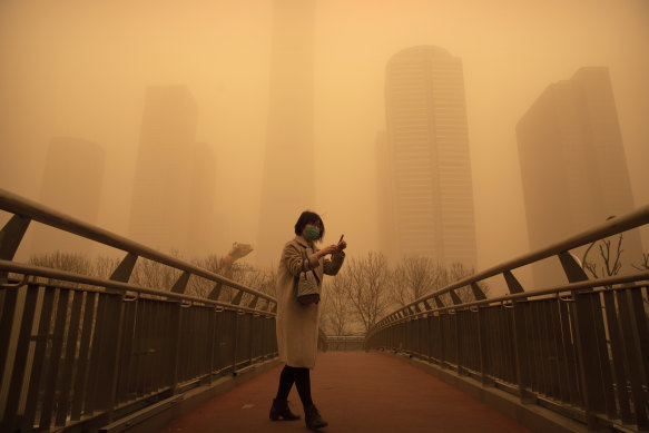 A woman walks along a pedestrian bridge amid a sandstorm in Beijing on Monday. 