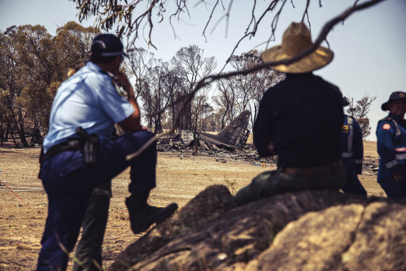 Police and other investigators watch from 
the shade of a tree near the crash site of the C-130.