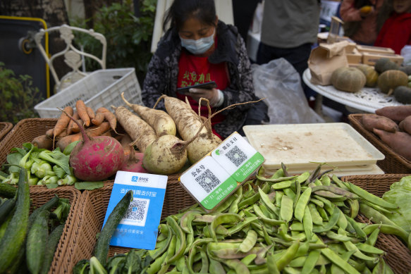 A vendor sits near cards displaying QR codes to pay electronically with Alipay and WeChat Pay at a farmer’s market in Beijing.