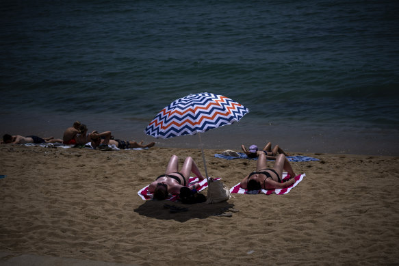 People sunbathe on a beach in Barcelona, Spain.