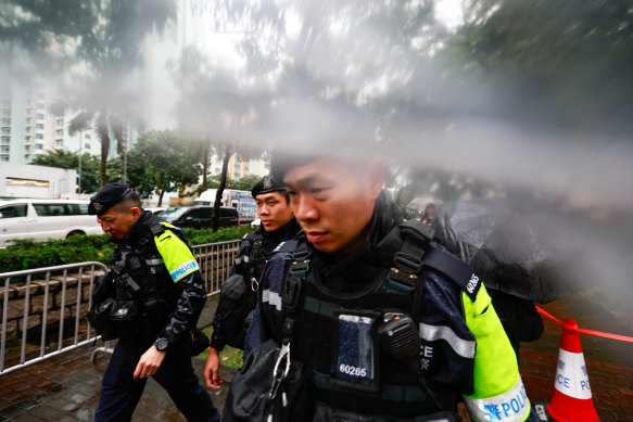 Armed police officers patrol as people wait in heavy rain for public gallery seats at the sentencing of Jimmy Lai who was convicted of violating the Beijing-imposed national security law, outside West Kowloon Magistrates’ Court.