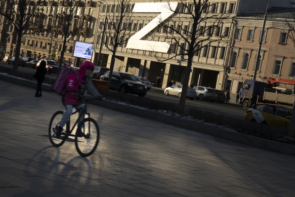 A food delivery courier rides a bicycle along a street with a huge letter Z, which has become a symbol of the Russian military, on a building during sunset in Moscow, Russia.