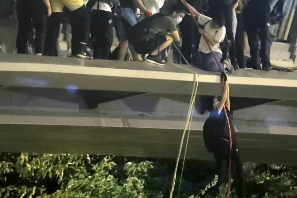 Protesters use a rope to lower themselves from a pedestrian bridge to waiting motorbikes.