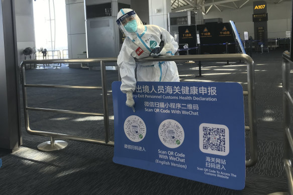 A worker in protective gear points to a QR code he must scan to make health declarations for inbound travelers arriving at Guangzhou Baiyun Airport in south China's Guangdong.