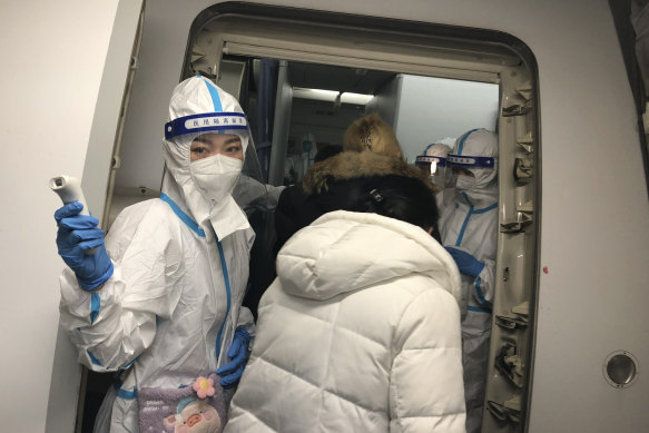 Cabin crew wearing protective gear check the temperatures of travellers heading to China on a flight from New York.