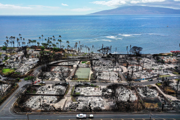 A recovery vehicle drives past burned structures and cars this month, after a devastating wildfire in Lahaina, Maui two months ago.