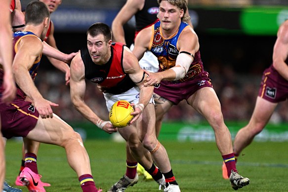 Zach Merrett of the Bombers attempts to break free from the defence of Will Ashcroft of the Lions.