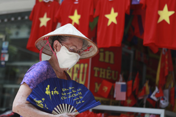 A woman walks past a row of T-shirts printed with Vietnamese flags in Hanoi. For 99 days, Vietnam seemed to have defeated the coronavirus, but now a new outbreak in the city of Da Nang has grown to dozens of cases in six cities.