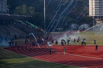 Students try to clear the tear gas canisters fired by riot police on the sports track during a confrontation in the Chinese University in Hong Kong.
