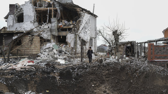 A woman stands on top of a crater next to a destroyed house.
