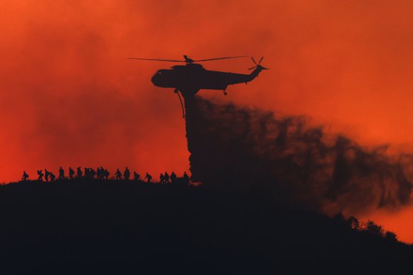 A water tanker drops water while firefighters walk below, as the Sandy Fire approaches in Simi Valley, California.