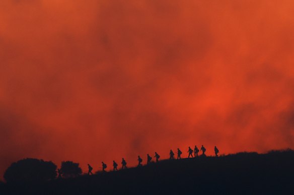 Firefighters are silhouetted walking amid the firing operation to control the Sandy Fire, Tuesday, May 19, 2026, in Simi Valley, California.