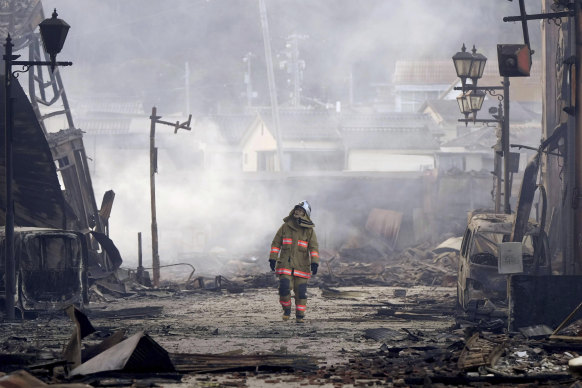A firefighter looks up the rubble and wreckage of a burnt-out marketplace following an earthquake in Wajima.