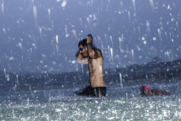 A swimmer braves the water at Bondi as a downpour sweeps across the beach on Thursday morning.
