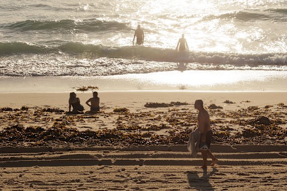 Early-morning bathers pick their way around piles of seaweed at Coogee Beach on Sunday.
