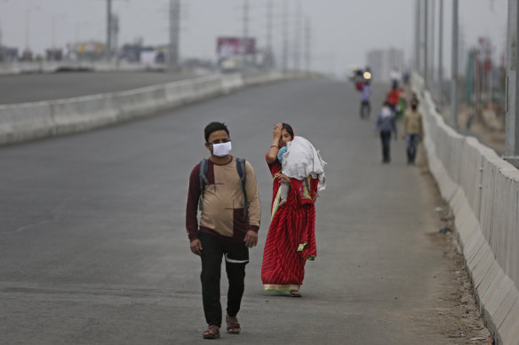 An Indian couple carrying an infant walk along an expressway hoping to reach their home, hundreds of kilometres away, as the city comes under lockdown in Ghaziabad, on the outskirts of Delhi.