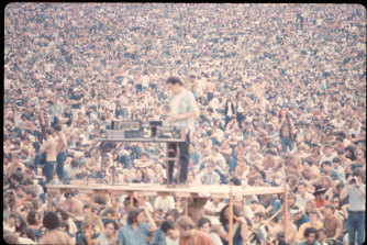 A sound guy stands on scaffolding with his equipment in front of the crowd at the Woodstock music festival, August 1969.
