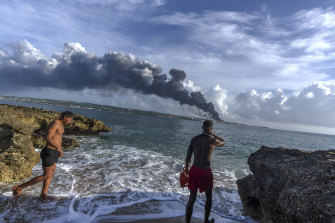 Sunbathers watch a huge plume of smoke rise from the Matanzas supertanker ba<em></em>se, as firefighters work to douse a fire that started during a thunderstorm the night before, in Matanzas, Cuba.