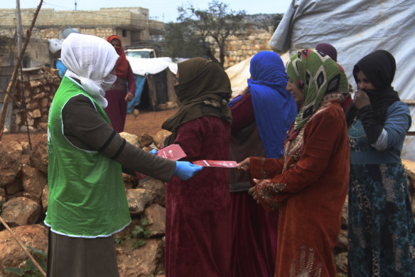 An aid worker with the Turkish humanitarian group IHH distributes  instructions on how to avoid coronavirus infection to Syrian women at a camp for internally displaced persons in northern Syria.