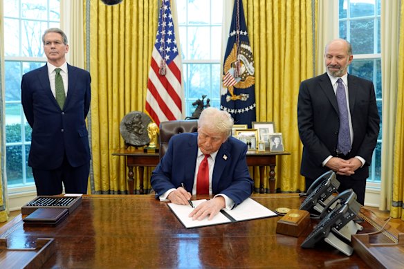 Donald Trump signs an executive order as Scott Bessent, left, and Howard Lutnick look on.