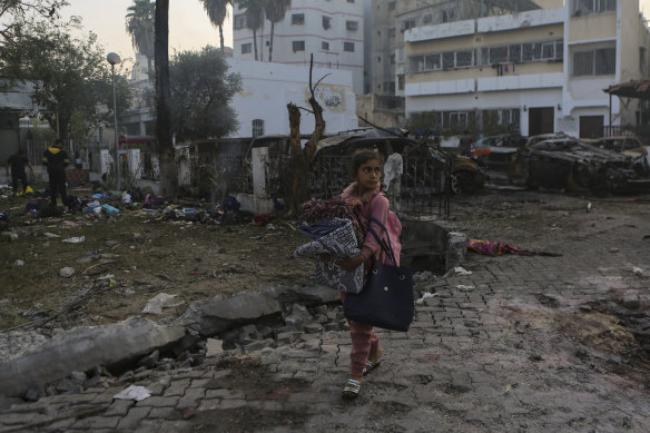 A Palestinian girl carries blankets as she walks past the explosion scene at Al Ahli hospital, in Gaza City.