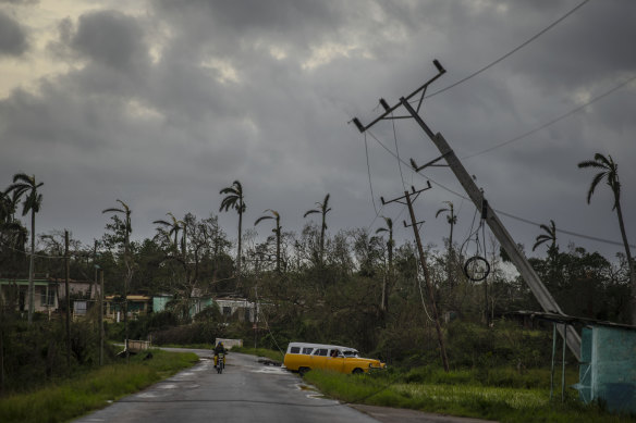 A classic American car drives past utility poles tilted by Hurricane Ian in Pinar del Rio, Cuba.