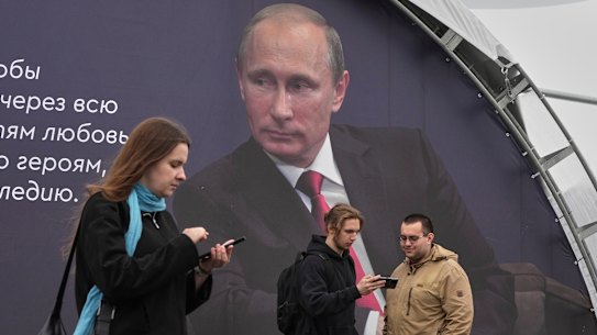 People at a book festival in St Petersburg walk in front of a poster of Russian President Vladimir Putin on Thursday.