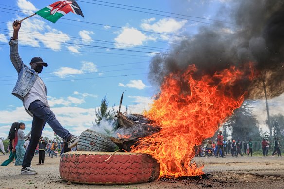 A protester raises a Kenyan flag near a burning barricade during a demonstration against a proposed Ebola quarantine center to be established by the United States at Laikipia Air Base in Nanyuki, Kenya.