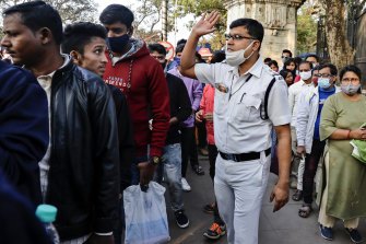 A policeman, wearing a face mask incorrectly, reprimands someone for not wearing a face mask as people line up to enter a park on New Year’s Day in Kolkata, India.
