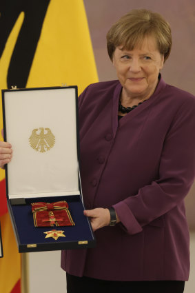 Former German chancellor Angela Merkel holds up the Order of Merit of the Federal Republic of Germany, the country’s highest accolade.