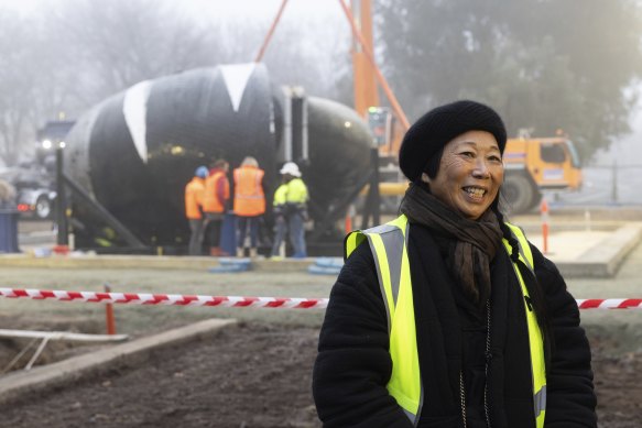 Artist Lindy Lee with her sculpture, Ouroboros, as it was craned into position at the front of the National Gallery of Australia, in Canberra early on Wednesday morning.