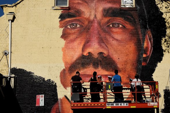 A group of artists paint a mural of Adam Goodes on the wall of a building on the corner of Foveaux Street and Crown Street in Surry Hills.