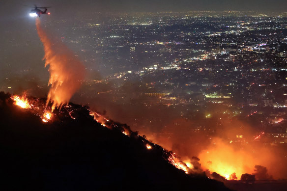A firefighting helicopter drops water as the Sunset fire burns in the Hollywood Hills.