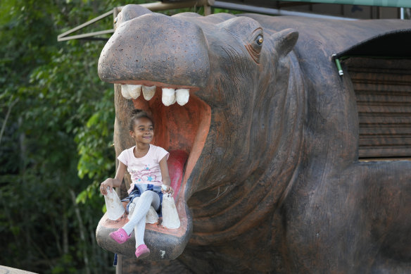 A girl poses for a photo on a statue of a hippo at the entrance of Hacienda Napoles.