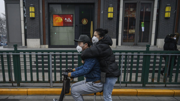 A Chinese couple wear protective masks as they ride a scooter in Beijing on Thursday.