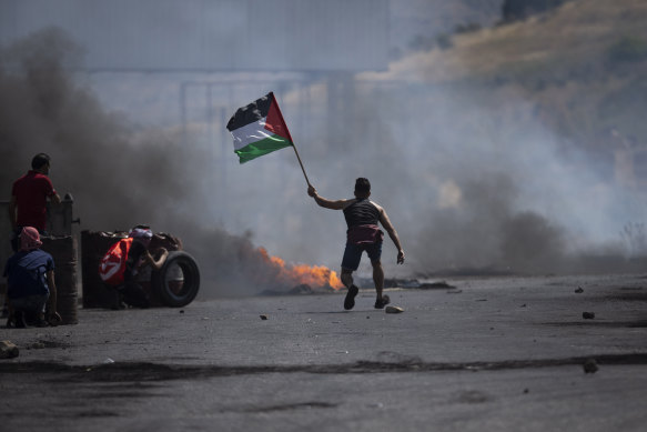 A protester waves the Palestinian flag during clashes with the Israeli forces at the Hawara checkpoint.