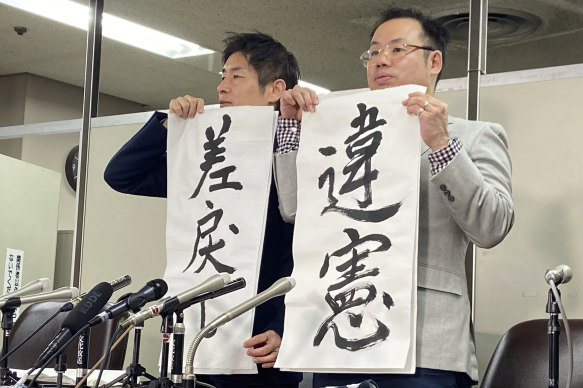 Lawyers Kazuyuki Minami, left, and Masafumi Yoshida hold signs that read “Unconstitutional”, right, and “Back (to High Court)” during a press conference following the ruling on Wednesday.