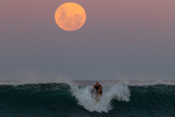 A surfer rides a wave as a super blood moon rises above the horizon at Manly Beach in May 2021.